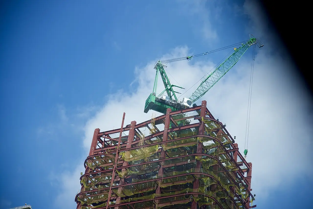 Structural steel frame under construction with a tower crane above